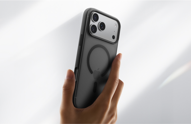 Hand holding an iPhone in a dark MagSafe-compatible case, showing the magnetic ring and triple camera setup against a bright background.