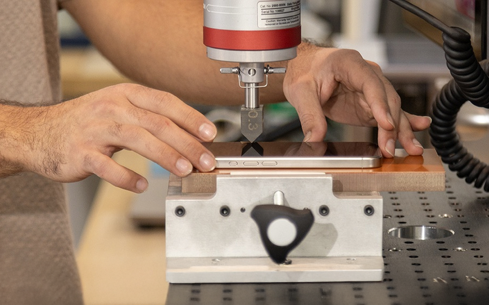 Close-up of a person testing a smartphone&rsquo;s durability using precision lab equipment that applies pressure to the screen.